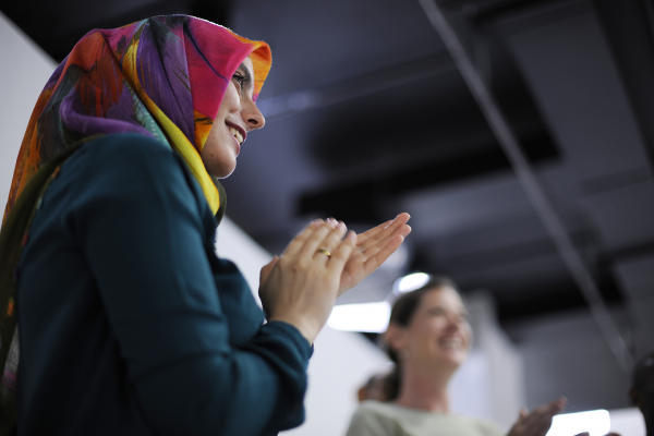 Two women clapping. The woman in the foreground is wearing a bright and colorful head scarf.
